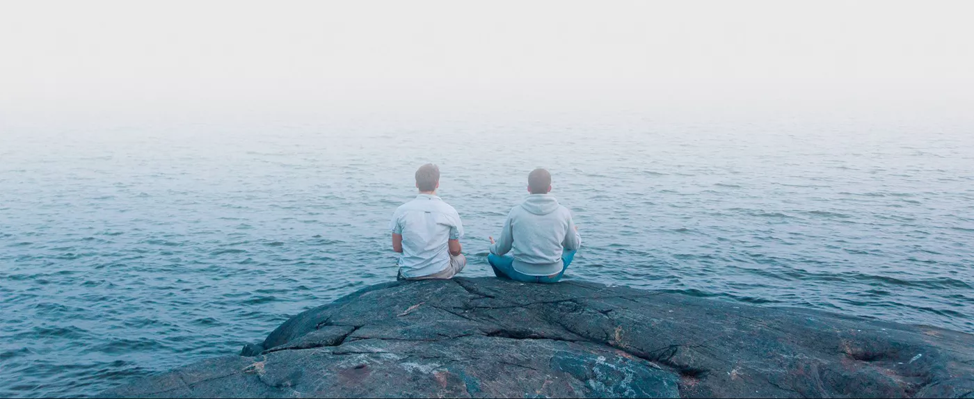 Due persone meditano su uno scoglio davanti al mare